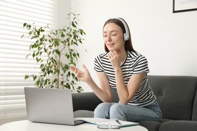 Photo of Smiling woman having online lesson with teacher by laptop at table indoors