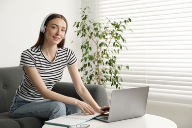 Photo of Smiling woman learning online using laptop at table on sofa indoors, space for text. Self-study