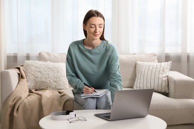 Photo of Woman taking notes during online lesson at table indoors. Self-study