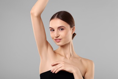 Photo of Young woman showing smooth skin after epilation on gray background