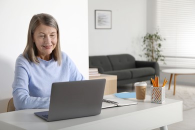 Photo of Smiling woman learning online using laptop at table indoors. Self-study