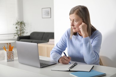 Photo of Woman learning online using laptop and taking notes at table indoors. Self-study