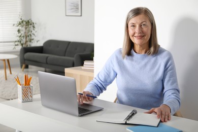 Photo of Smiling woman learning online using laptop at table indoors. Self-study