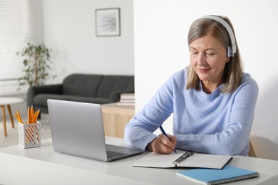 Photo of Woman learning online using laptop and taking notes at table indoors. Self-study