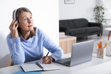 Photo of Woman learning online using laptop and taking notes at table indoors. Self-study