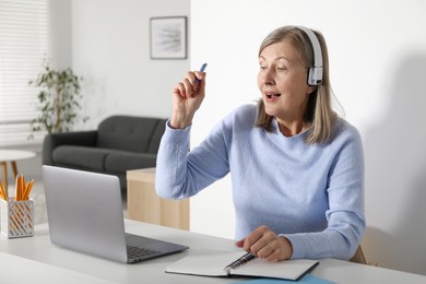 Photo of Emotional woman learning online using laptop at table indoors. Self-study