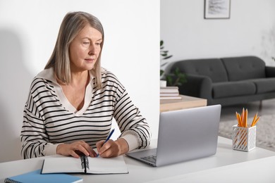 Photo of Woman learning online using laptop and taking notes at table indoors. Self-study