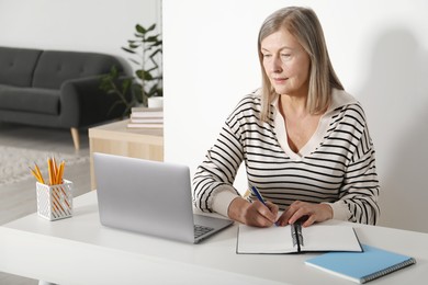 Photo of Woman learning online using laptop and taking notes at table indoors. Self-study