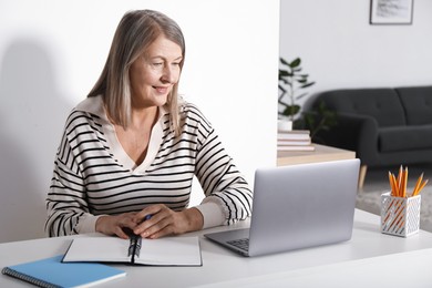 Photo of Smiling woman learning online using laptop at table indoors. Self-study