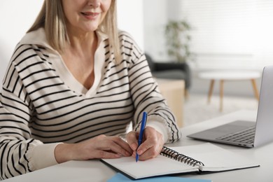 Photo of Woman learning online using laptop and taking notes at table indoors, closeup. Self-study