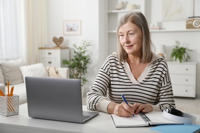 Photo of Woman learning online using laptop and taking notes at table indoors. Self-study