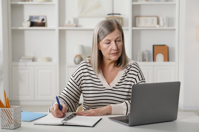 Photo of Woman learning online using laptop and taking notes at table indoors. Self-study