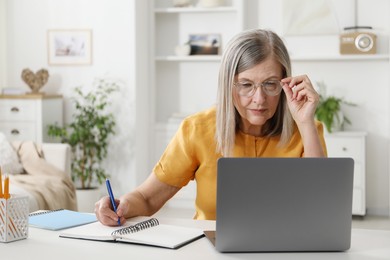 Photo of Woman learning online using laptop and taking notes at table indoors. Self-study