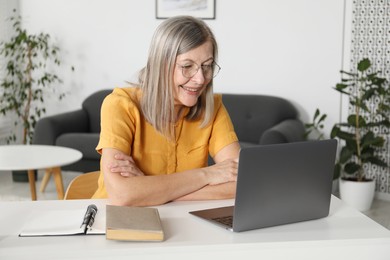 Photo of Smiling woman learning online using laptop at table indoors. Self-study