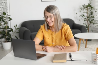 Photo of Smiling woman learning online using laptop at table indoors. Self-study