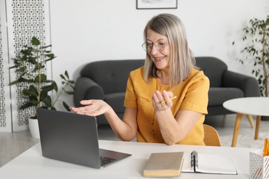 Photo of Smiling woman having online lesson with teacher by laptop at table indoors