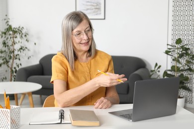 Photo of Smiling woman having online lesson with teacher by laptop at table indoors