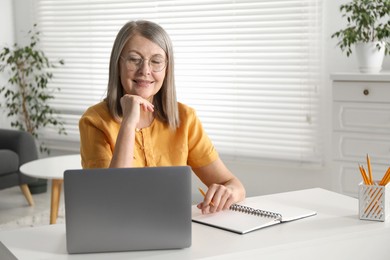 Photo of Smiling woman learning online using laptop at table indoors. Self-study