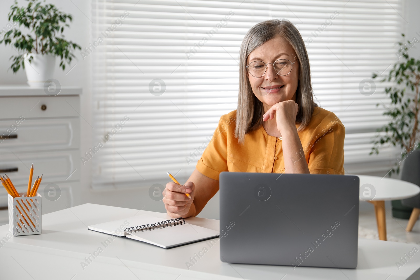 Photo of Smiling woman learning online using laptop at table indoors. Self-study