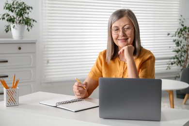 Photo of Smiling woman learning online using laptop at table indoors. Self-study