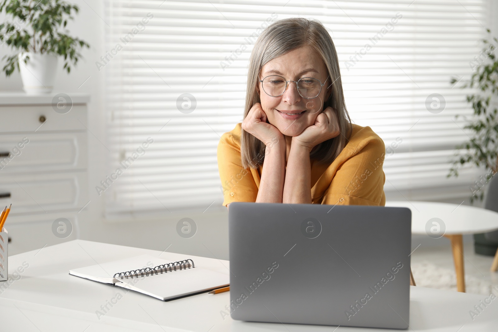 Photo of Smiling woman learning online using laptop at table indoors. Self-study