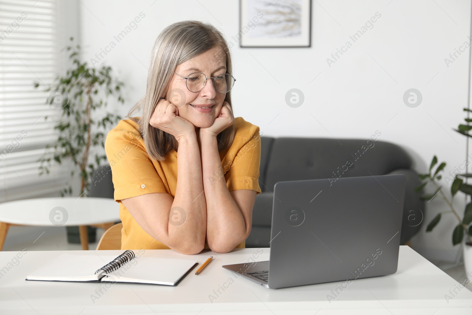 Photo of Smiling woman learning online using laptop at table indoors. Self-study