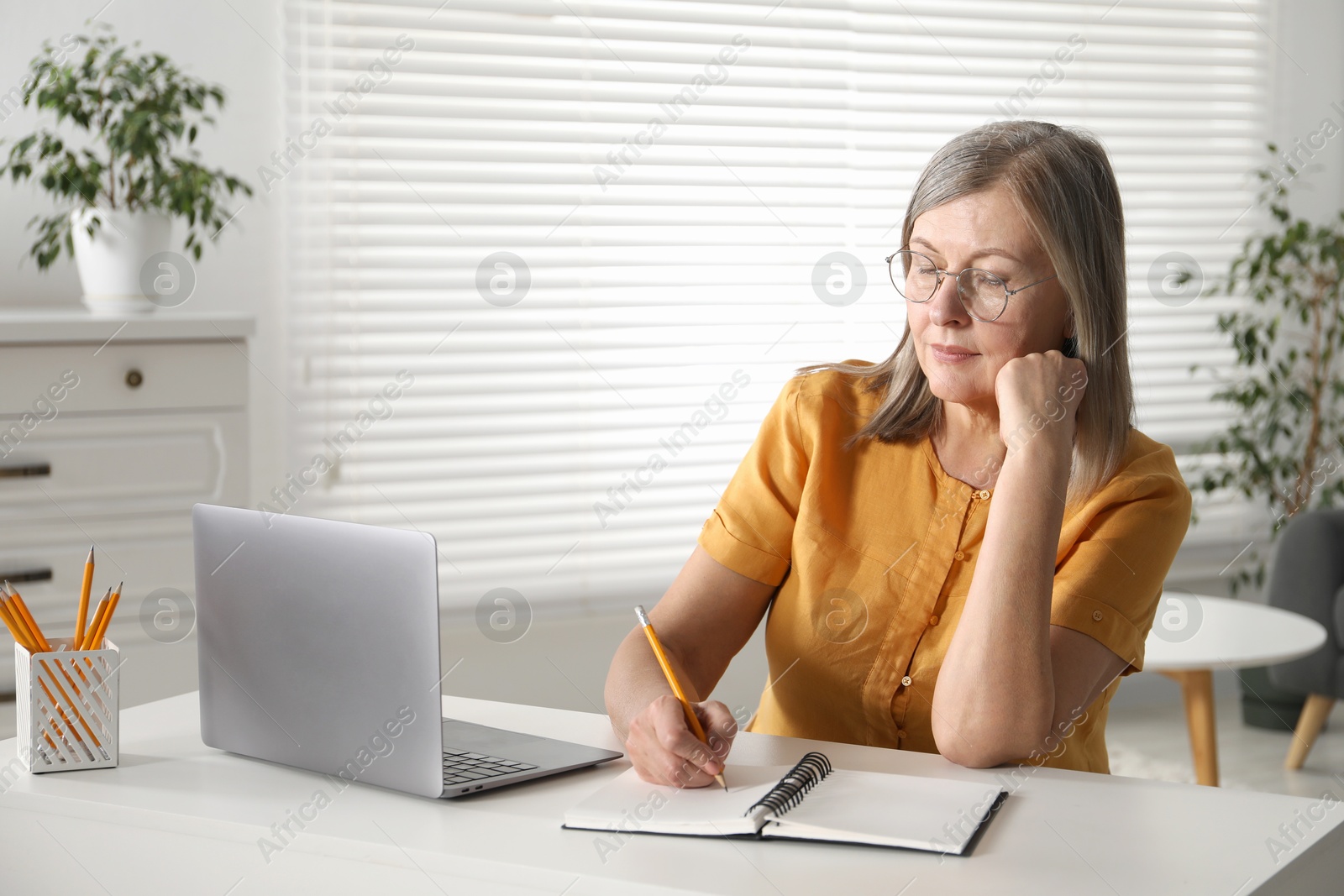 Photo of Woman learning online using laptop and taking notes at table indoors. Self-study