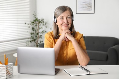 Photo of Smiling woman learning online using laptop at table indoors. Self-study