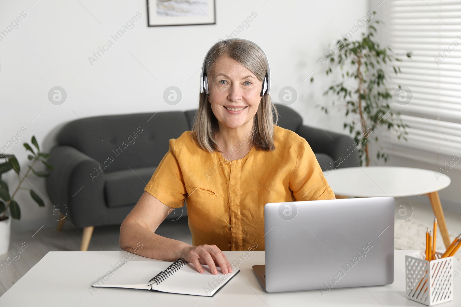 Photo of Smiling woman learning online using laptop at table indoors. Self-study