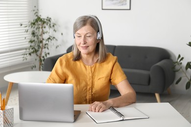 Photo of Smiling woman learning online using laptop at table indoors. Self-study