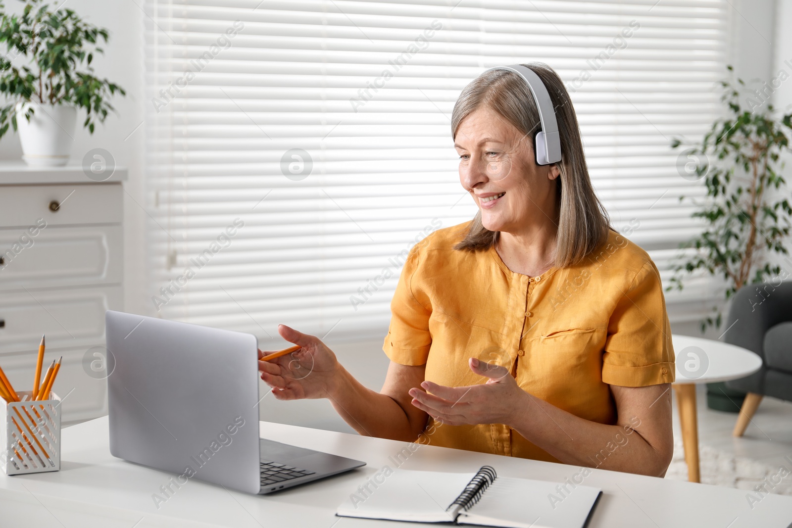 Photo of Smiling woman having online lesson with teacher by laptop at table indoors