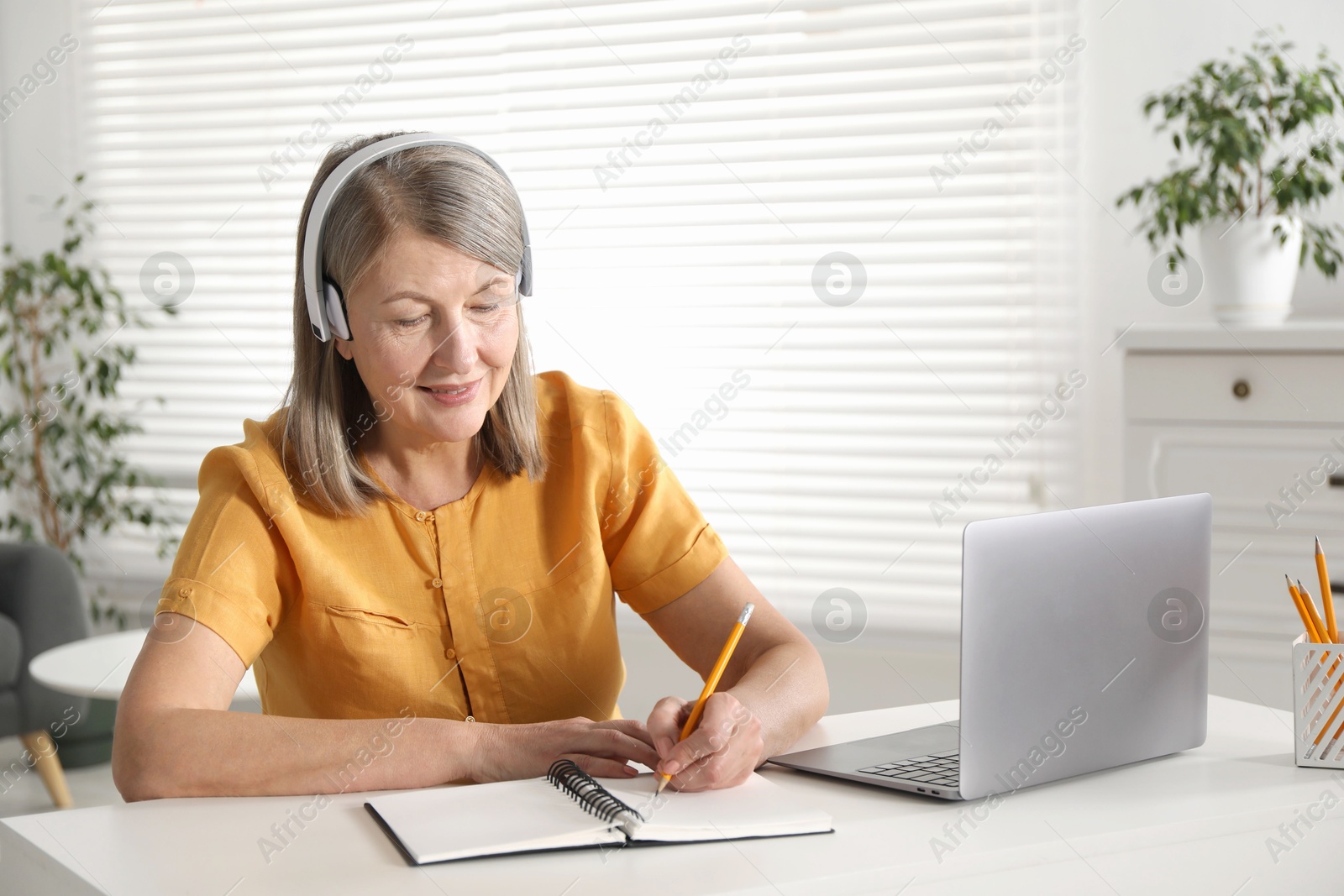 Photo of Woman learning online using laptop and taking notes at table indoors. Self-study