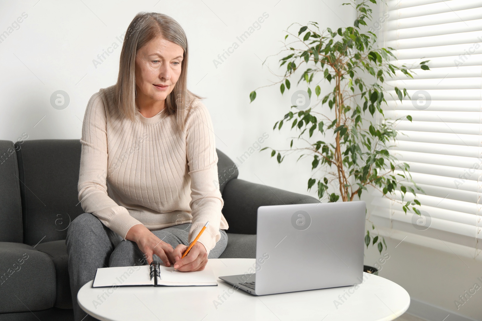 Photo of Woman learning online using laptop and taking notes at table indoors. Self-study