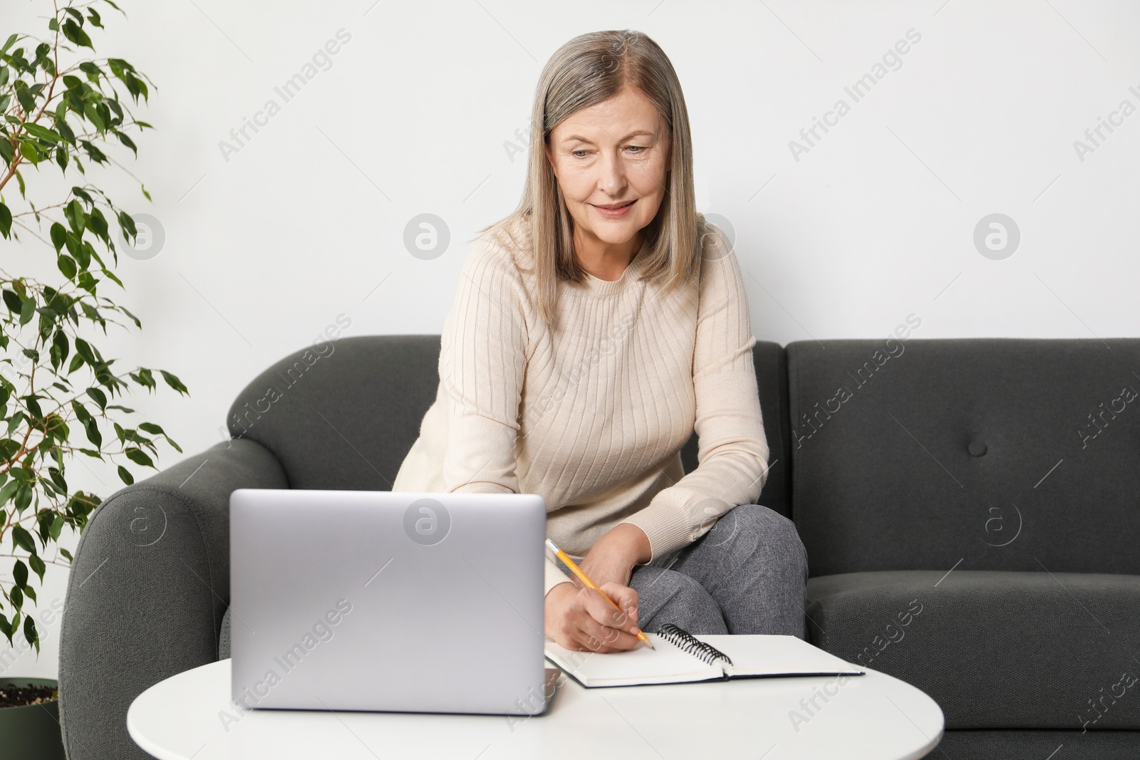 Photo of Woman learning online using laptop and taking notes at table indoors. Self-study