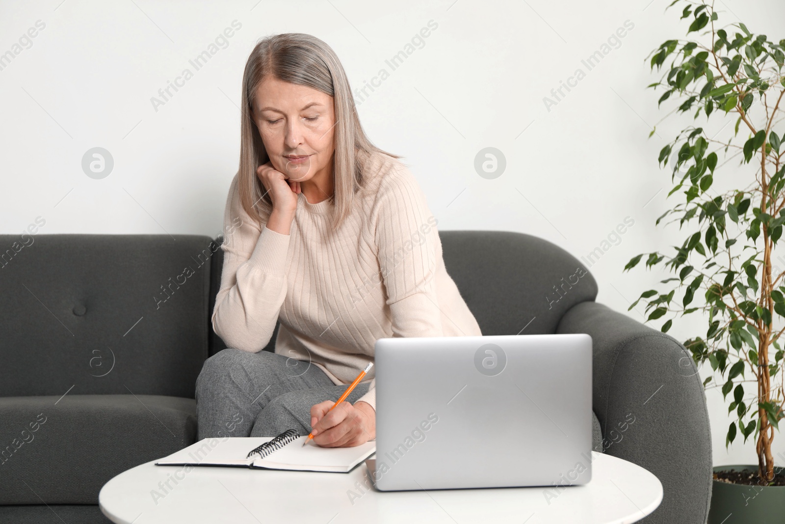 Photo of Woman learning online using laptop and taking notes at table indoors. Self-study