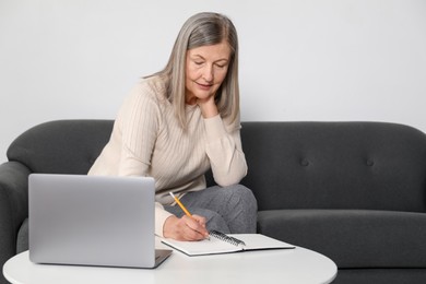 Photo of Woman learning online using laptop and taking notes at table indoors. Self-study