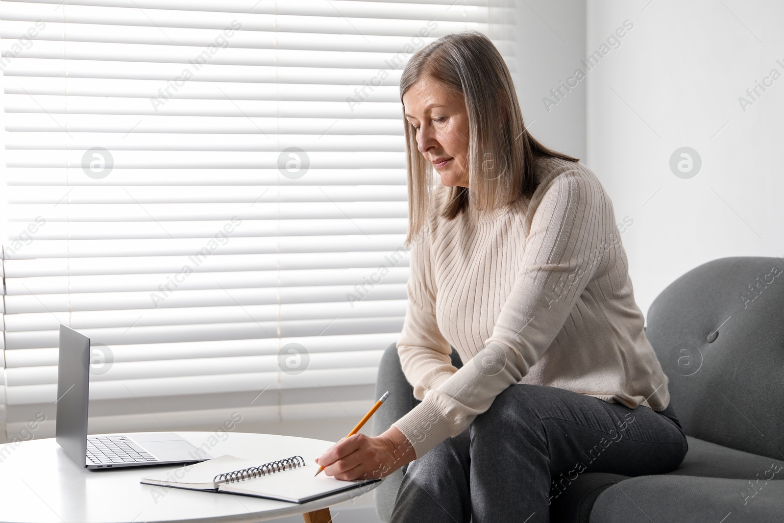 Photo of Woman learning online using laptop and taking notes at table indoors. Self-study