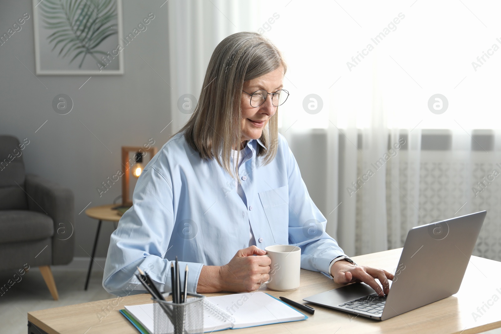 Photo of Woman with cup learning online using laptop at table indoors. Self-study