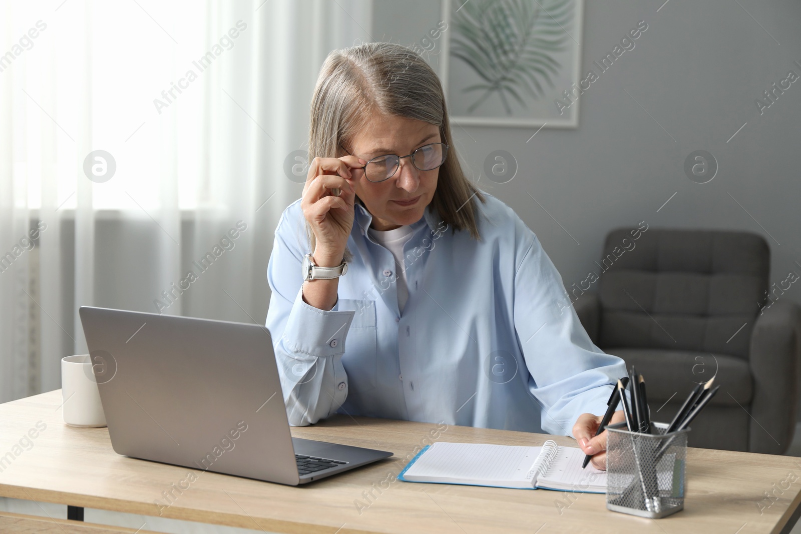 Photo of Woman learning online using laptop and taking notes at table indoors. Self-study