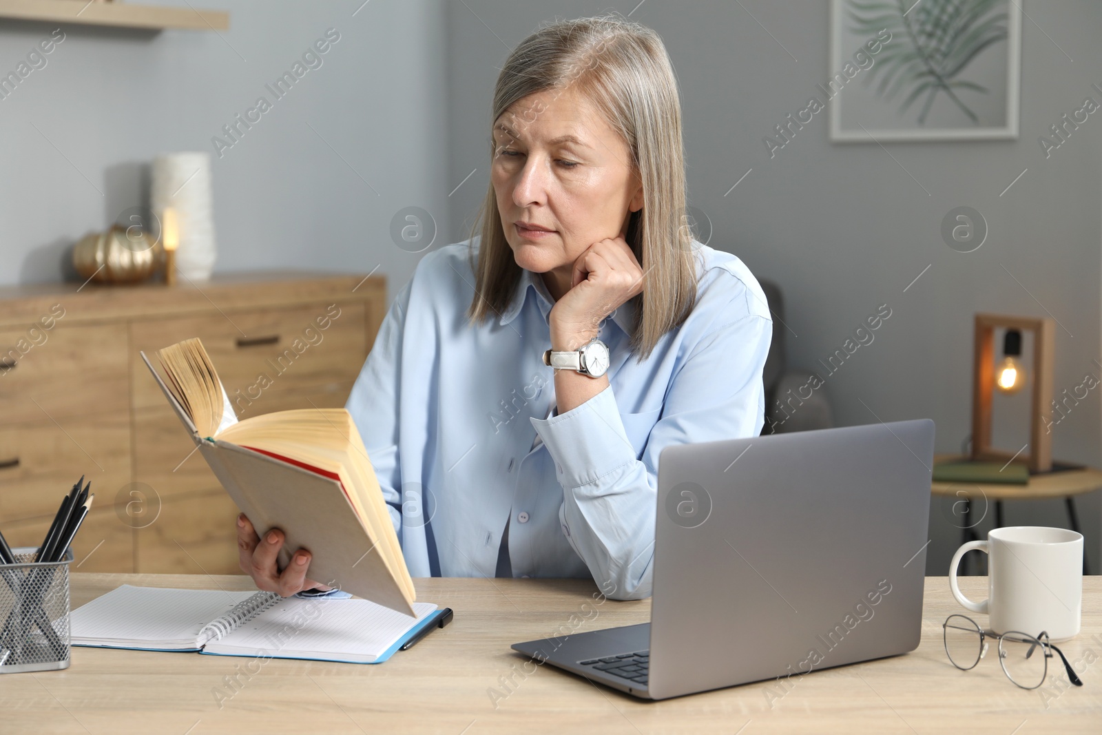 Photo of Woman with book learning near laptop at table indoors. Self-study