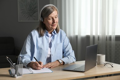 Photo of Woman learning online using laptop and taking notes at table indoors. Self-study