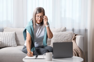 Photo of Woman learning online using laptop and taking notes at table indoors. Self-study