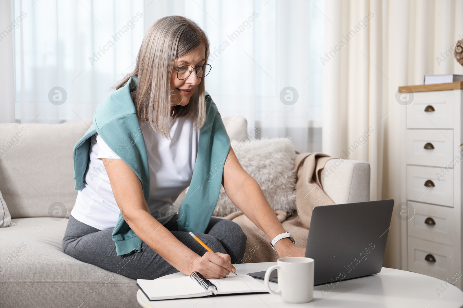 Photo of Woman learning online using laptop and taking notes at table indoors. Self-study