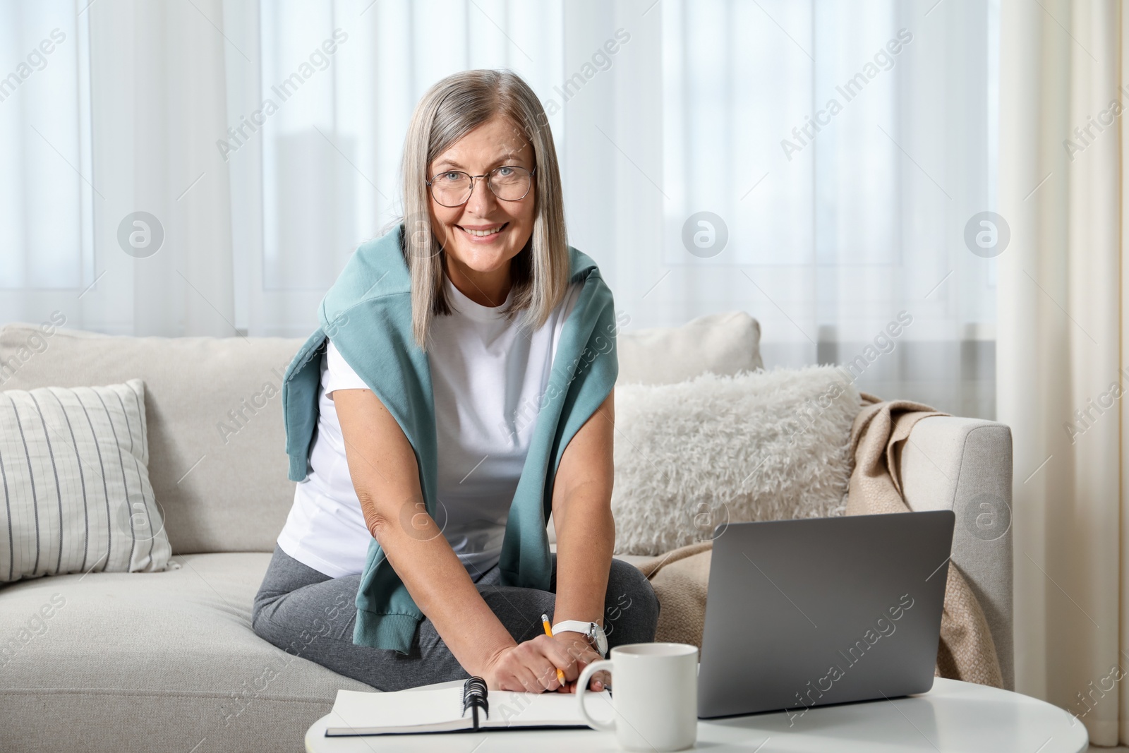 Photo of Smiling woman learning online using laptop at table indoors. Self-study