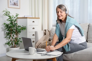 Photo of Smiling woman learning online using laptop at table indoors. Self-study