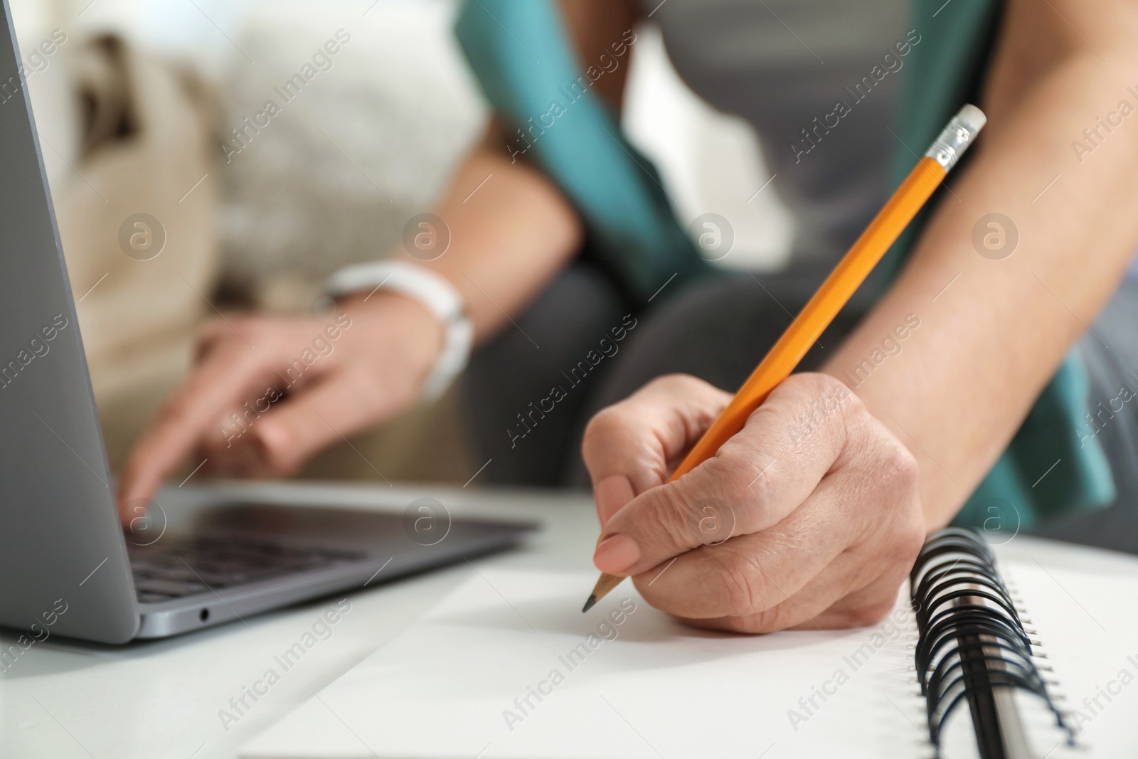 Photo of Woman learning online using laptop and taking notes at white table indoors, closeup. Self-study