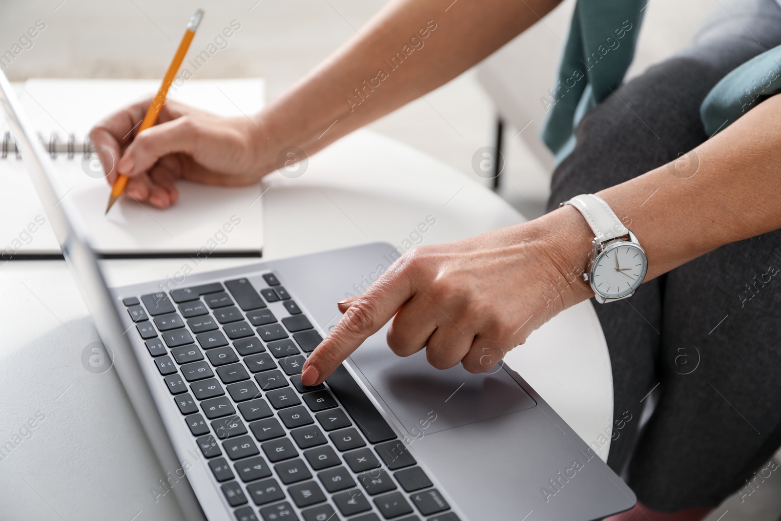 Photo of Woman learning online using laptop and taking notes at white table indoors, closeup. Self-study