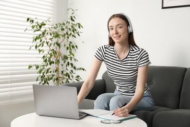 Photo of Smiling woman taking notes during online lesson at table indoors. Self-study