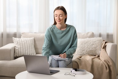 Photo of Woman taking notes during online lesson at table indoors. Self-study