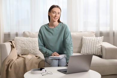 Photo of Smiling woman learning online using laptop at table on sofa indoors. Self-study